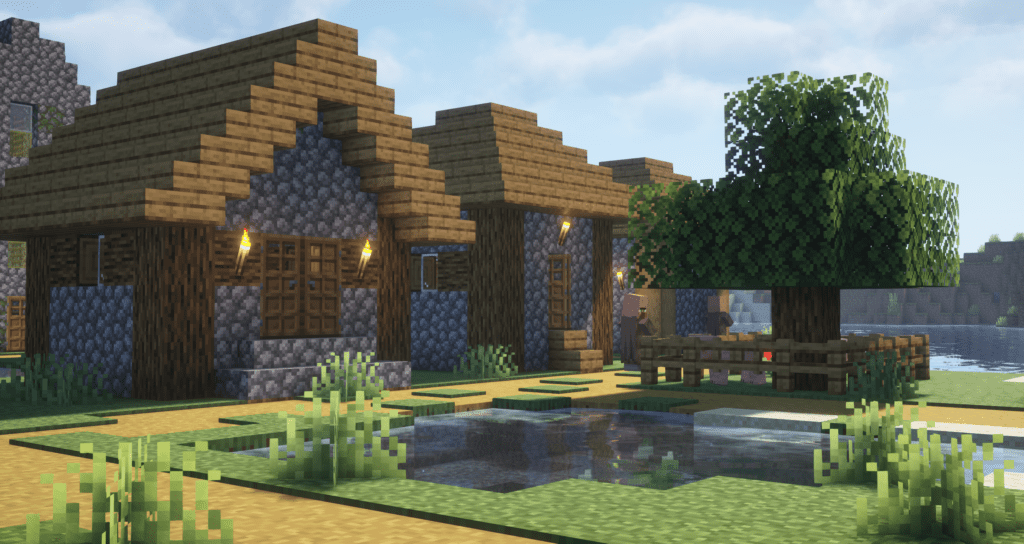 A bright and vibrant Minecraft village enhanced with Complementary Unbound Shaders. The sunlight casts realistic shadows, while the reflections in the water add depth and realism. The wooden houses and stone textures appear crisp and detailed, with soft ambient lighting enhancing the scene. The lush greenery and clear blue sky create a warm and inviting atmosphere.